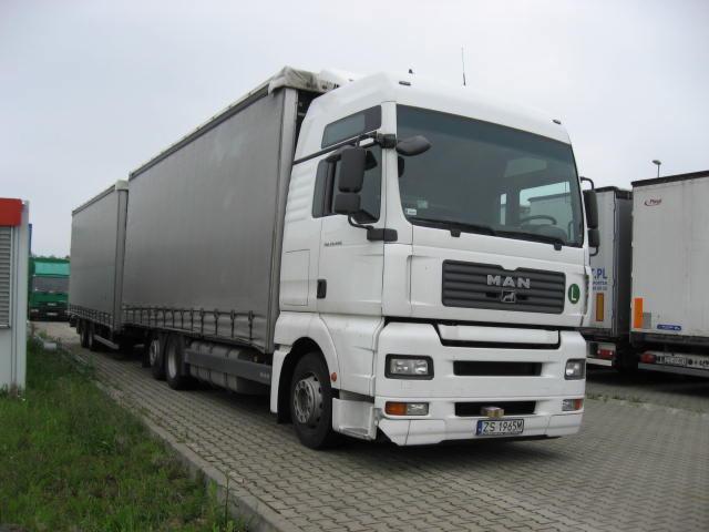 Biały ciągnik siodłowy MAN z naczepą typu firanka na parkingu z kostki brukowej, widoczny numer rejestracyjny ZS 1965M.