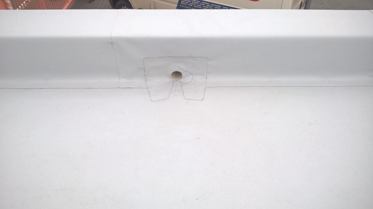 Biała membrana dachowa z wyciętym otworem na element instalacji, widoczny fragment pojazdu w tle.