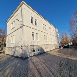 Trzypiętrowy budynek po renowacji elewacji, widok z dołu w słoneczny dzień, z widocznymi oknami i rynnami.