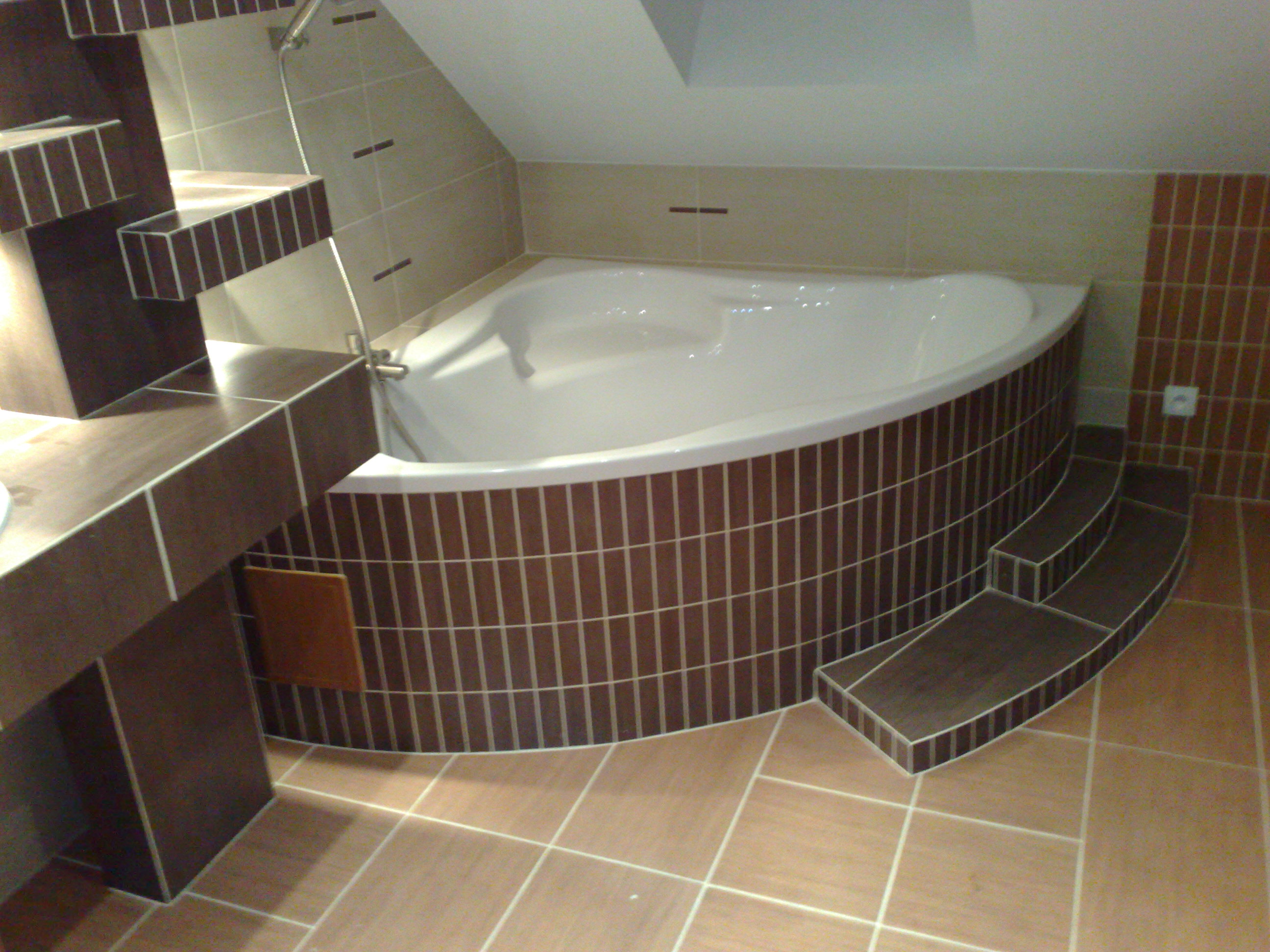 Wykończona łazienka w poddaszu ze szczegółową zabudową wanny z brązowych płytek, widoczne schodki wejściowe do wanny i półki z płytek.