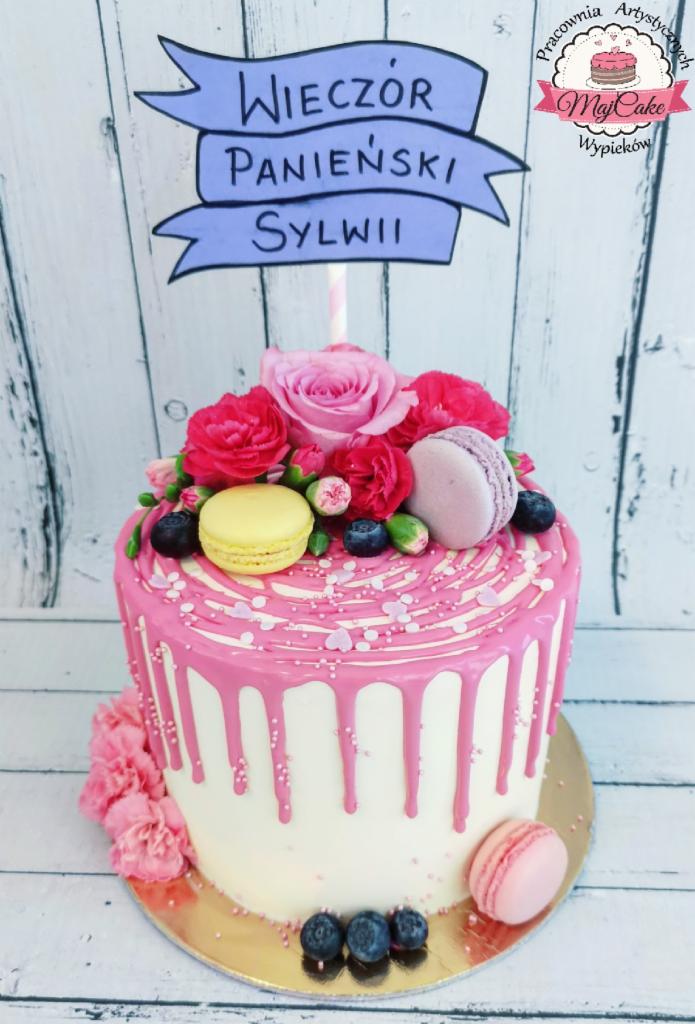 Tort na wieczór panieński z różami, makaronikami i borówkami, ozdobiony różowym lukrem spływającym po bokach.