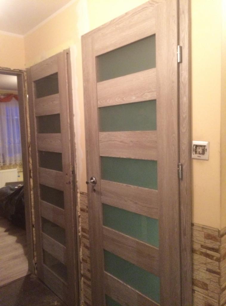 Dwa zamontowane, szklane drzwi wewnętrzne w odcieniach szarości w mieszkaniu w Rumi, widoczne niedoskonałości wykończenia ścian.