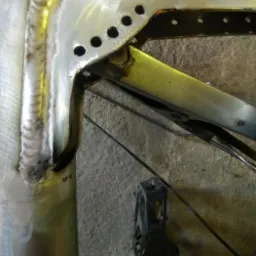 Detale spoin na metalowej ramie roweru, widoczne ślady obróbki i otwory montażowe.