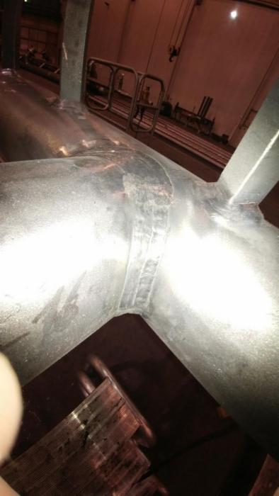 Spoina na metalowej rurze w kształcie litery Y, widoczna w hali przemysłowej, z widocznymi śladami obróbki i niedoskonałościami powierzchni.