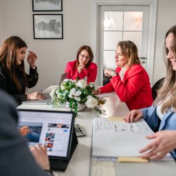 MERITUM BIURO RACHUNKOWE DR KLAUDIA KOZŁOWSKA - Zespół biura rachunkowego przy pracy: przeglądanie dokumentów, praca na laptopie i tablecie, w tle dekoracja kwiatowa i grafiki na ścianie.