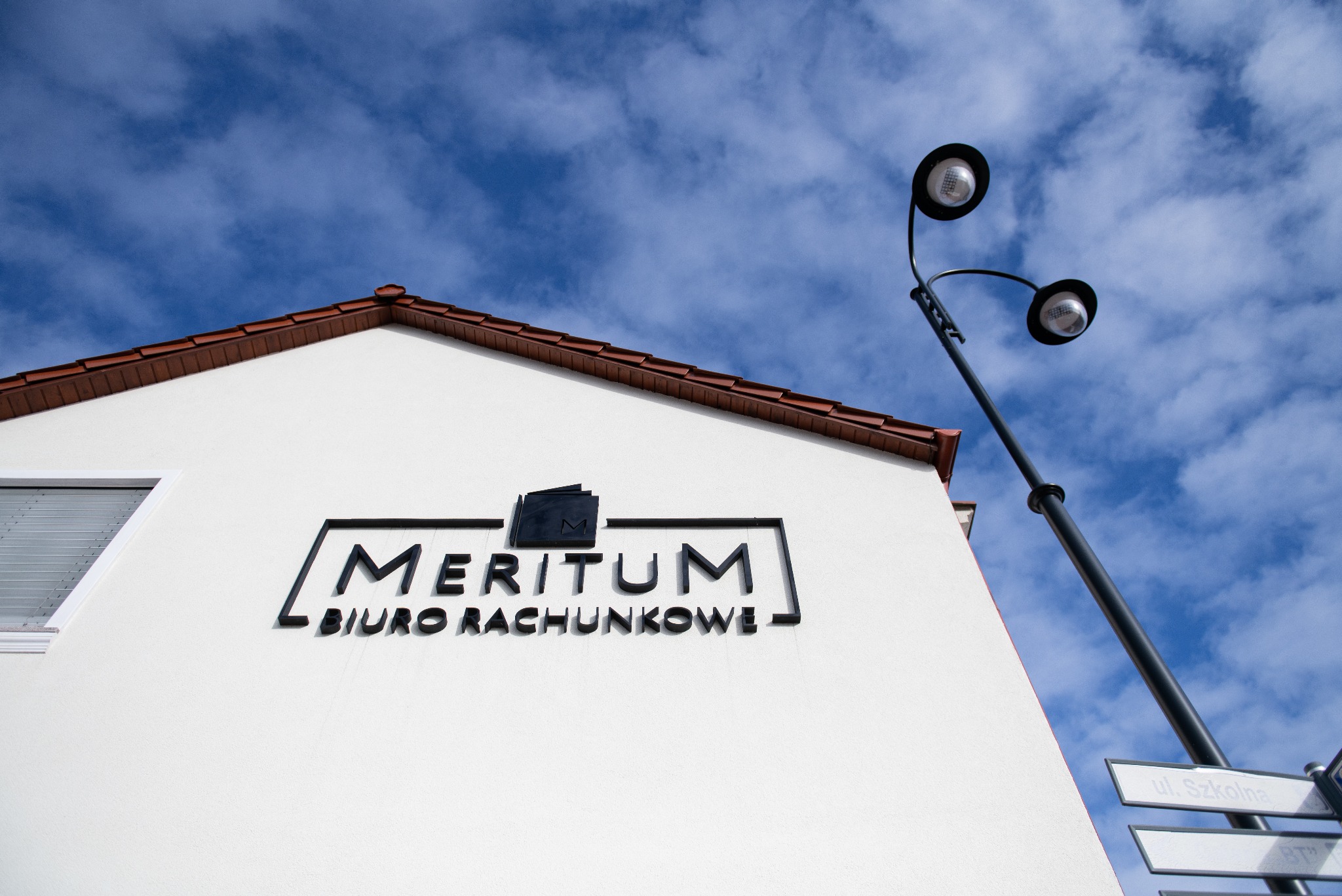Budynek biura rachunkowego Meritum w Tucholi z logo i adresem na tle błękitnego nieba. Ujęcie z dołu podkreśla nowoczesny wygląd siedziby firmy.