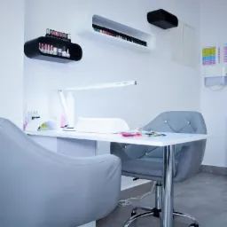 Stanowisko do manicure z lampą UV, próbnikami kolorów i półkami na lakiery w minimalistycznym, jasnym wnętrzu.