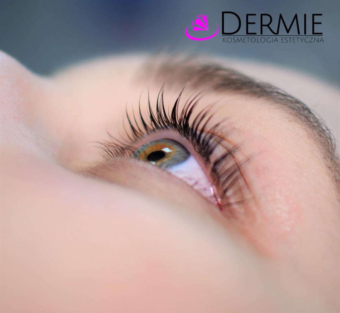Zbliżenie na oko z przedłużonymi rzęsami, widoczne logo 'DERMIE Kosmetologia Estetyczna' w górnej części kadru.