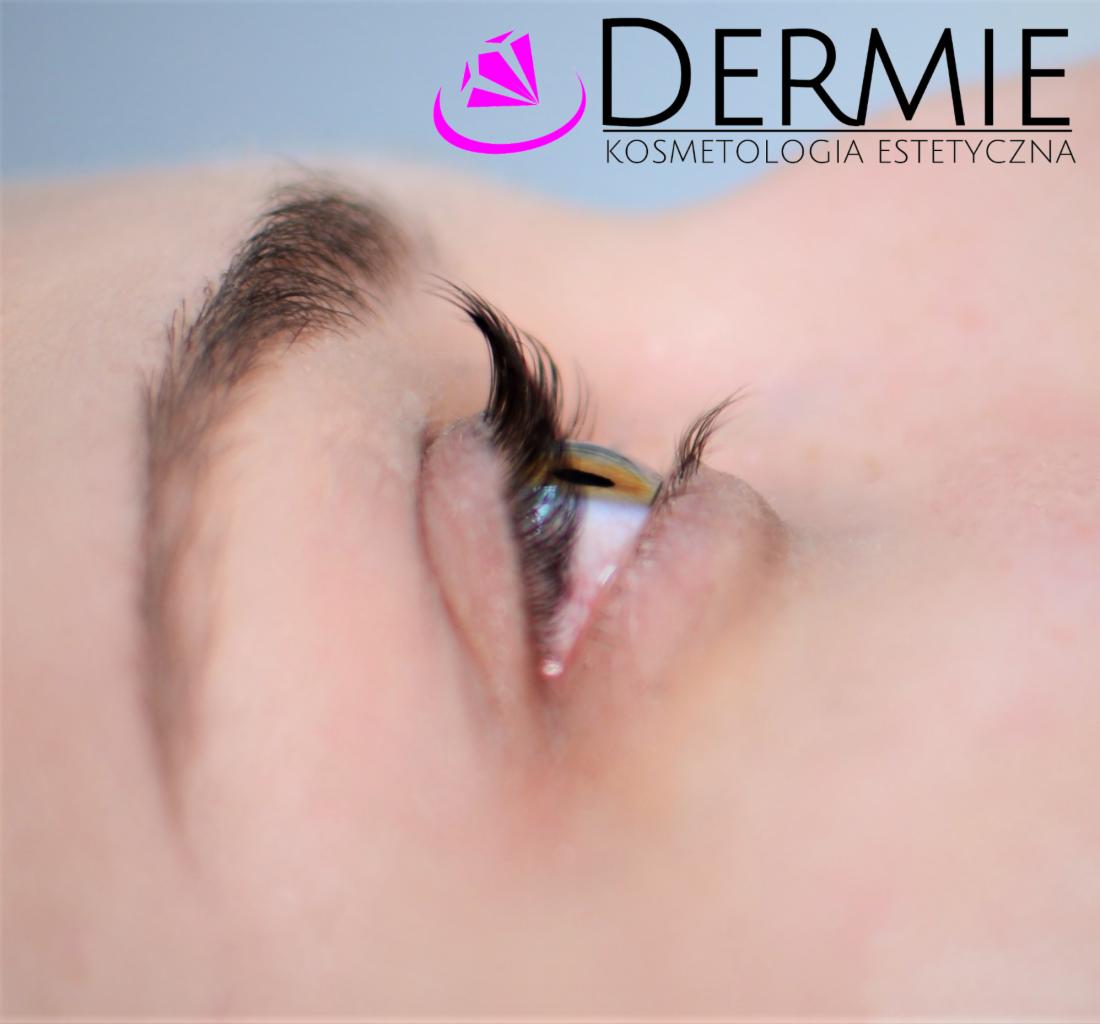 Zbliżenie na oko z wyraźnie podkreślonymi, długimi rzęsami, z logo firmy kosmetycznej w tle.