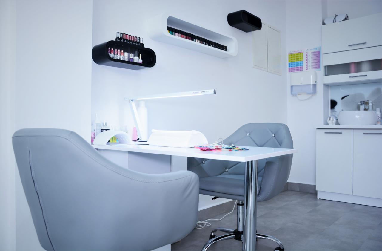 Stanowisko do manicure z lampą UV, próbnikami kolorów i półkami na lakiery w minimalistycznym, jasnym wnętrzu.