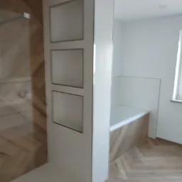 Nowoczesna łazienka z prysznicem typu walk-in i wanną obudowaną panelami drewnopodobnymi, z wnękami w ścianie wykończonymi na biało.