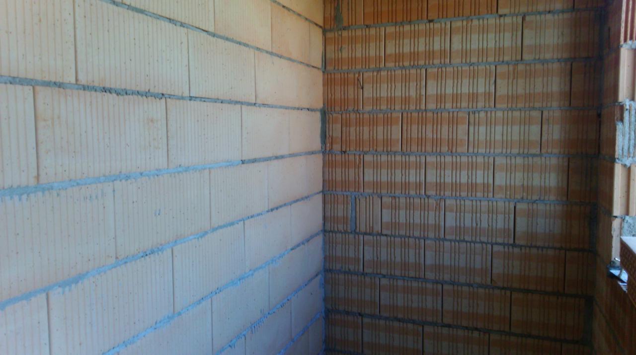 Wnętrze budynku w trakcie budowy, widoczny narożnik z wymurowanymi ścianami z bloczków ceramicznych o dwóch różnych odcieniach, połączonych szarą zaprawą.