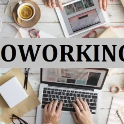 Widok z góry na jasne biurko z laptopem, tabletem, herbatą z cytryną, słodyczami i materiałami do pakowania prezentów, dłonie piszą na klawiaturze laptopa.