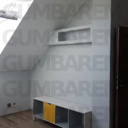 Pokój na poddaszu z ułożonymi panelami podłogowymi, pomalowanymi ścianami na szaro i białym regałem z żółtą szufladą.