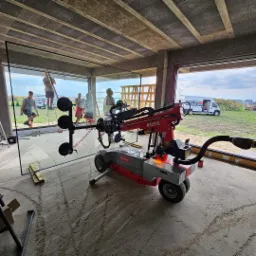 Montaż dużego okna z użyciem specjalistycznego podnośnika Befard w surowym stanie budynku; widoczni pracownicy i krajobraz na zewnątrz.