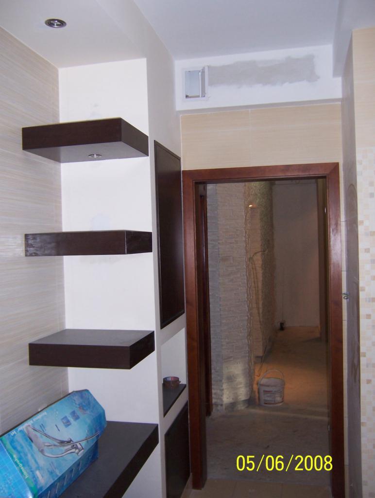 Wykończone wnętrze łazienki z płytkami, zabudową z półkami i otwartym przejściem do dalszej części. Widoczna data na zdjęciu.