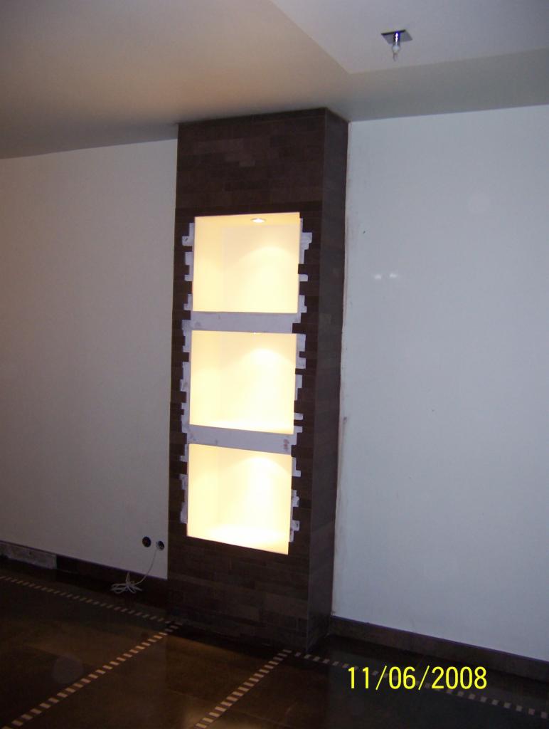 Narożna zabudowa z płytek imitujących drewno z trzema podświetlonymi wnękami w Chorzowie. Wnęki przygotowane pod montaż półek.