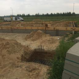 DNV Realiz LTD Sp. Z o.o. S.k - Budowa fundamentów domu jednorodzinnego: szalunki, zbrojenie, wykopane doły pod stopy fundamentowe, na drugim planie samochód dostawczy i zieleń.