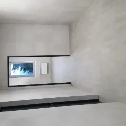 Wnętrze łazienki wykończone jasnymi, wielkoformatowymi płytkami ceramicznymi na ścianach i podłodze; widoczne okno z czarną ramą i wnęka w podłodze z czarnym obramowaniem.