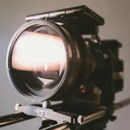 Profesjonalna kamera filmowa na szynach, obiektyw skierowany w stronę widza, widoczny czerwony wskaźnik, logo MTJ na podstawie.