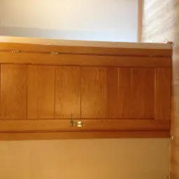 Drewniana szafka wisząca z haczykiem, zamontowana na ścianie w jasnym wnętrzu, widok z dołu.