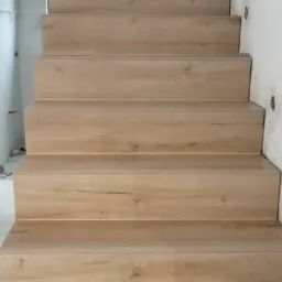 Schody wykończone panelami o wzorze jasnego drewna, widok z dołu, ściany w trakcie wykończenia.