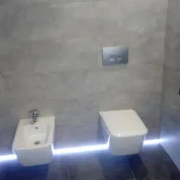 Nowoczesna łazienka z szarymi płytkami, podwieszanym bidetem i toaletą, oświetleniem LED pod urządzeniami i minimalistycznym panelem sterującym spłuczką.