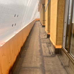 Usługi Blacharsko-Dekarskie - Dach pokryty papą termozgrzewalną, zabezpieczony folią ochronną. Widoczne ocieplenie ścian budynku wełną mineralną. Prace dekarskie w toku, detale wykończeniowe.