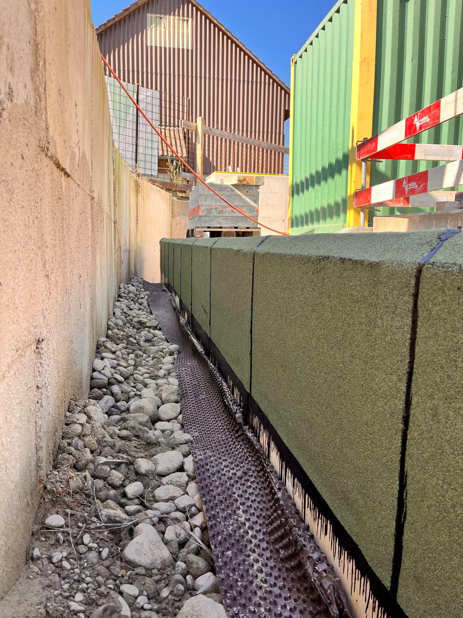 Izolacja fundamentów budynku z użyciem zielonych płyt izolacyjnych i folii kubełkowej, widok z bliska na drenaż i zabezpieczenie przed wilgocią.