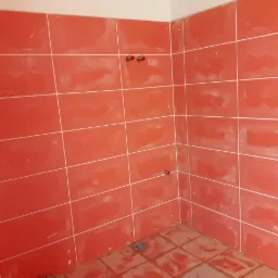 Świeżo położone, czerwone płytki ceramiczne z białymi fugami na ścianach i podłodze łazienki, widoczne wystające rury instalacji wodnej.