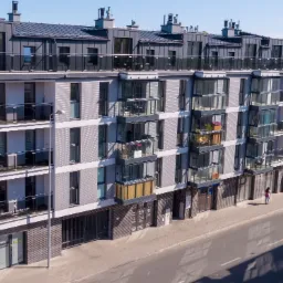 Nowoczesny budynek mieszkalny z balkonami i biurami na parterze, widok z góry na ulicę i przechodzącą osobę.