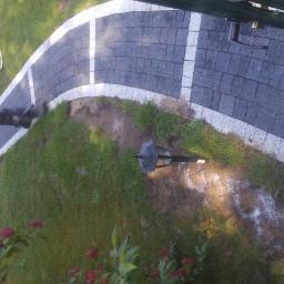 Radbruk - Zakrzywiona ścieżka z ciemnej kostki brukowej z białymi obrzeżami, widok z góry, w tle trawnik i osoby.