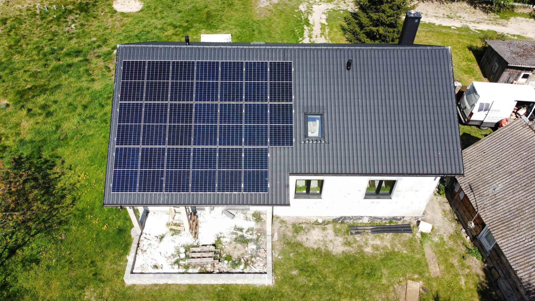 Widok z góry na dom z panelami słonecznymi na grafitowym dachu; na dole widoczny teren w trakcie prac wykończeniowych.