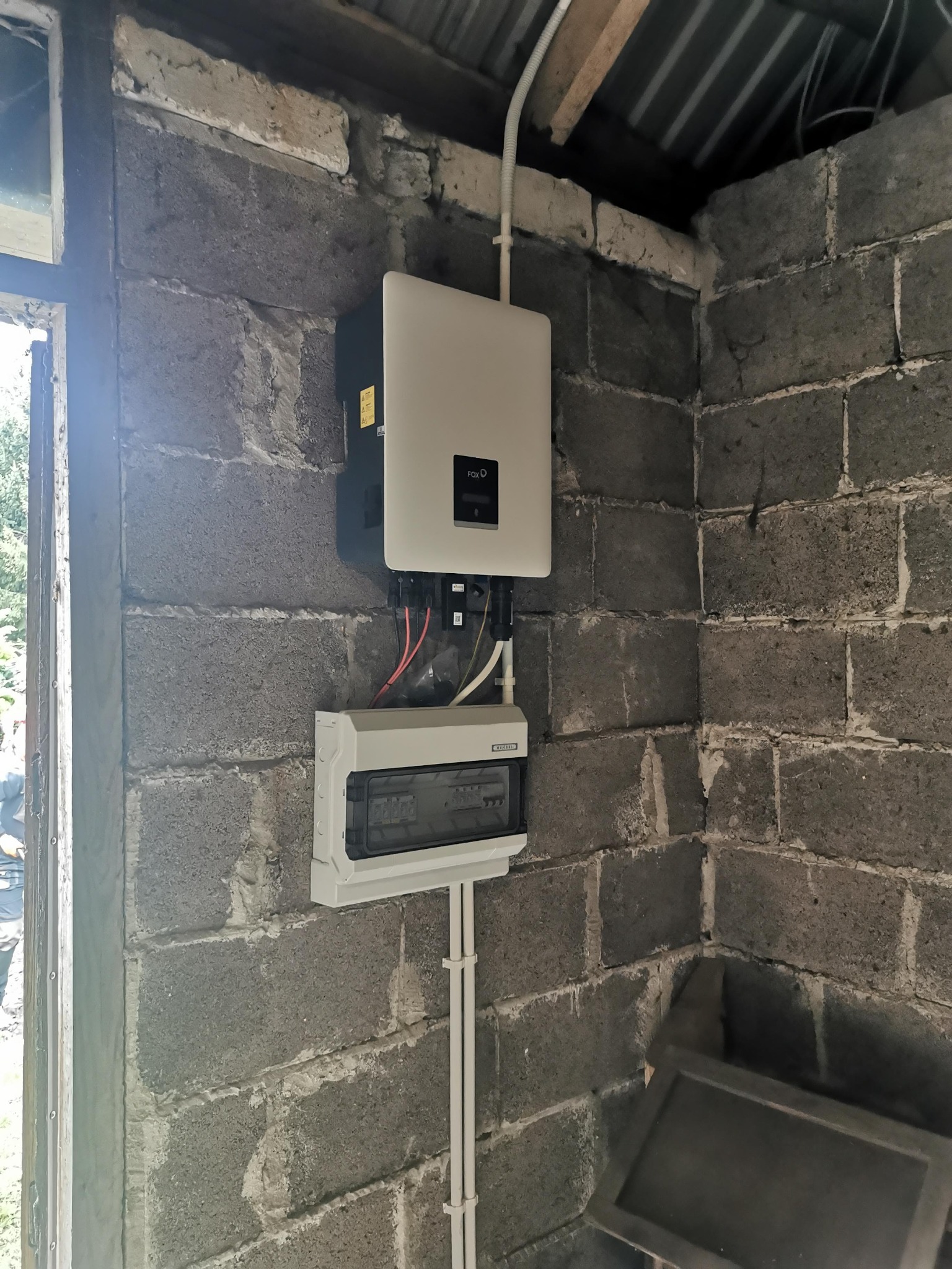 Zamontowany inwerter i skrzynka zabezpieczeń na surowej ścianie z szarego betonu komórkowego wewnątrz budynku.