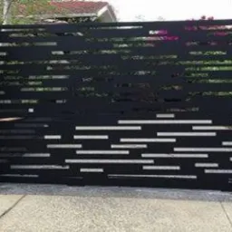 Nowoczesna brama wjazdowa z czarnego metalu z geometrycznym ażurowym wzorem poziomych pask&oacute;w, osadzona na drewnianych słupkach, sąsiadująca z drewnianym ogrodzeniem.