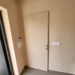 Beżowe, świeżo pomalowane wnętrze w Rawiczu z drzwiami wewnętrznymi, włącznikami światła i panelem alarmowym.