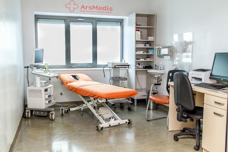 Jasne wnętrze gabinetu lekarskiego z pomarańczowym leżanką, aparaturą medyczną, biurkiem z komputerem i oknem z logo kliniki.