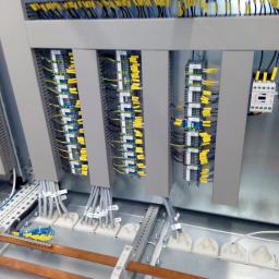 NAPTECH Dariusz Napieracz - Wnętrze rozdzielnicy elektrycznej z licznymi przewodami, złączkami i zabezpieczeniami, starannie ułożonymi i oznaczonymi, widoczne szyny uziemiające z miedzianymi elementami.