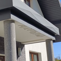 Firma TIMBER Artur Terpiłowski - Nowoczesny daszek nad wejściem do domu z szarej blachy trapezowej, wsparty na dwóch okrągłych, kamiennych kolumnach, z widocznymi śladami po kleju montażowym na spodniej stronie daszku.