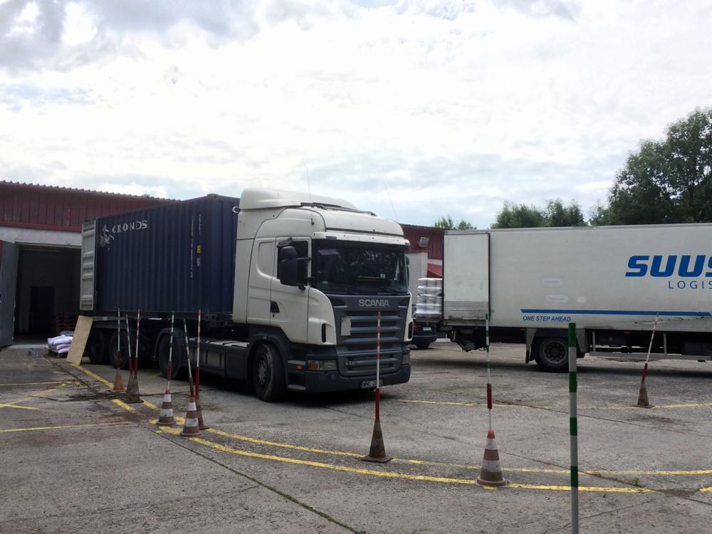 Ciężarówka SCANIA z kontenerem CEONDS na placu manewrowym z żółtymi liniami i pachołkami, obok zaparkowana naczepa SUUS Logistics.