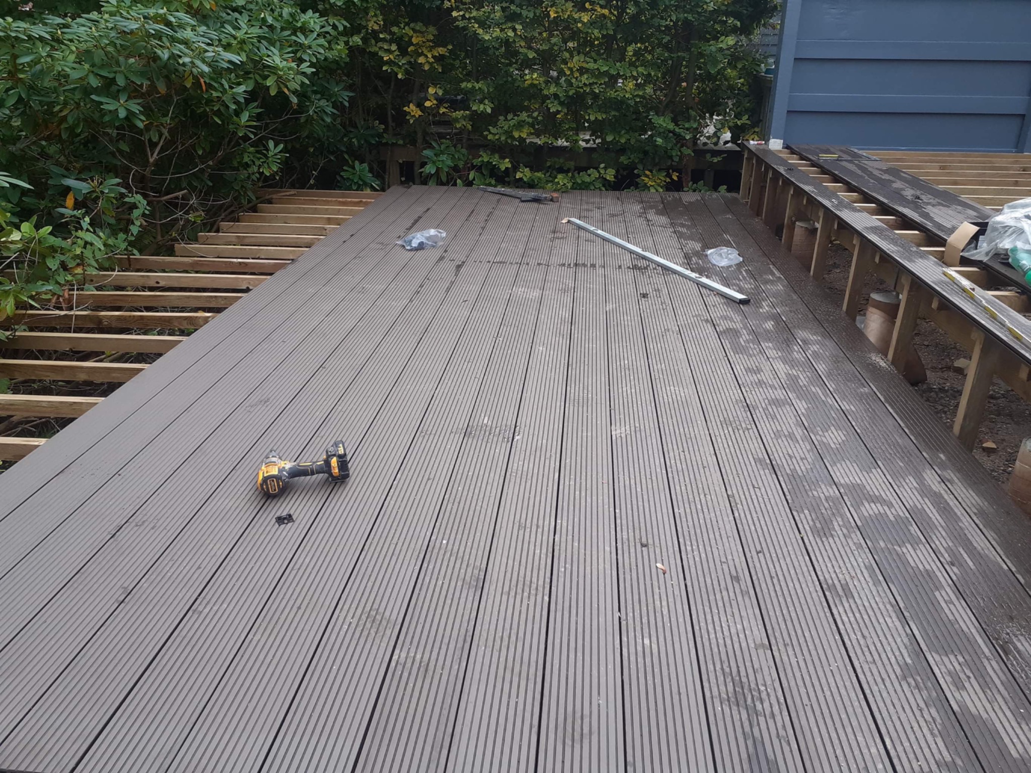 Budowa tarasu z desek kompozytowych w ogrodzie, widoczne legary, częściowo ułożona nawierzchnia, wkrętarka i poziomica.