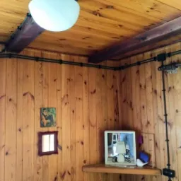 Wnętrze pokoju wykończonego boazerią z widocznymi, natynkowymi przewodami elektrycznymi w czarnej osłonie, biegnącymi wzdłuż ścian i sufitu, z lampą wiszącą, półką z lustrem i dekoracjami.