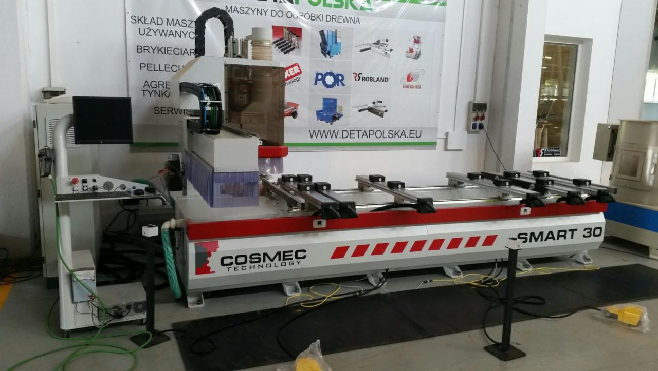 Centrum obróbcze CNC Cosmec Smart 30 do drewna w hali produkcyjnej, z widocznym panelem sterowania i osprzętem, na tle ściany z reklamami maszyn do obróbki drewna.