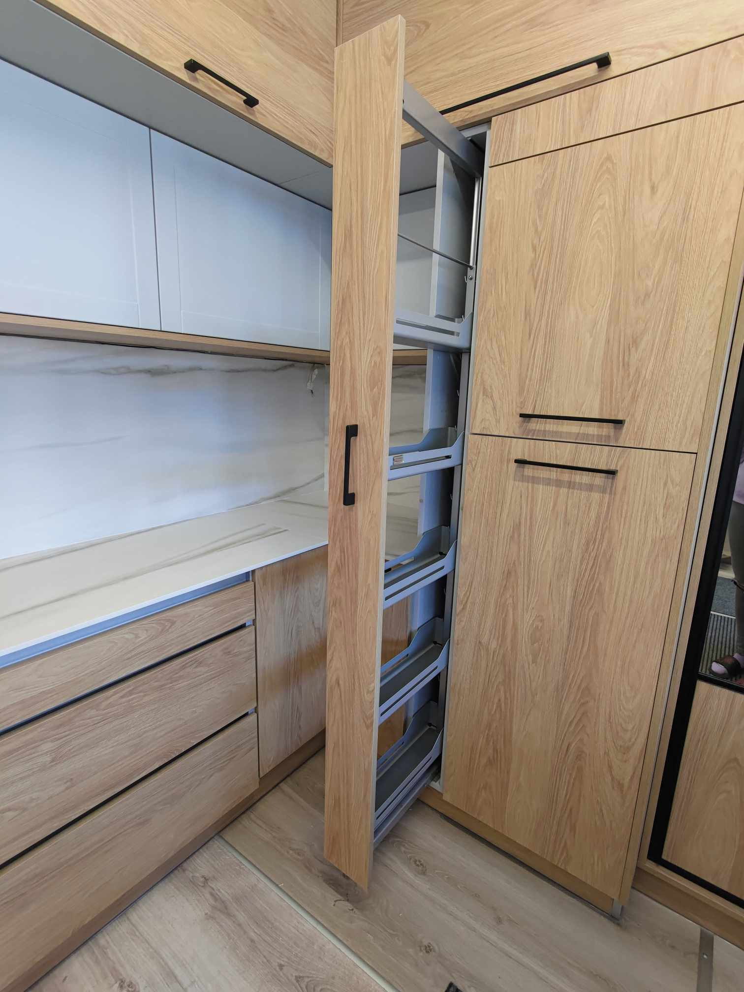 Jasna kuchnia na wymiar z drewnianymi frontami i wysuwaną szafką cargo. Minimalistyczne czarne uchwyty. Blat z imitacją marmuru. Nowoczesny design.