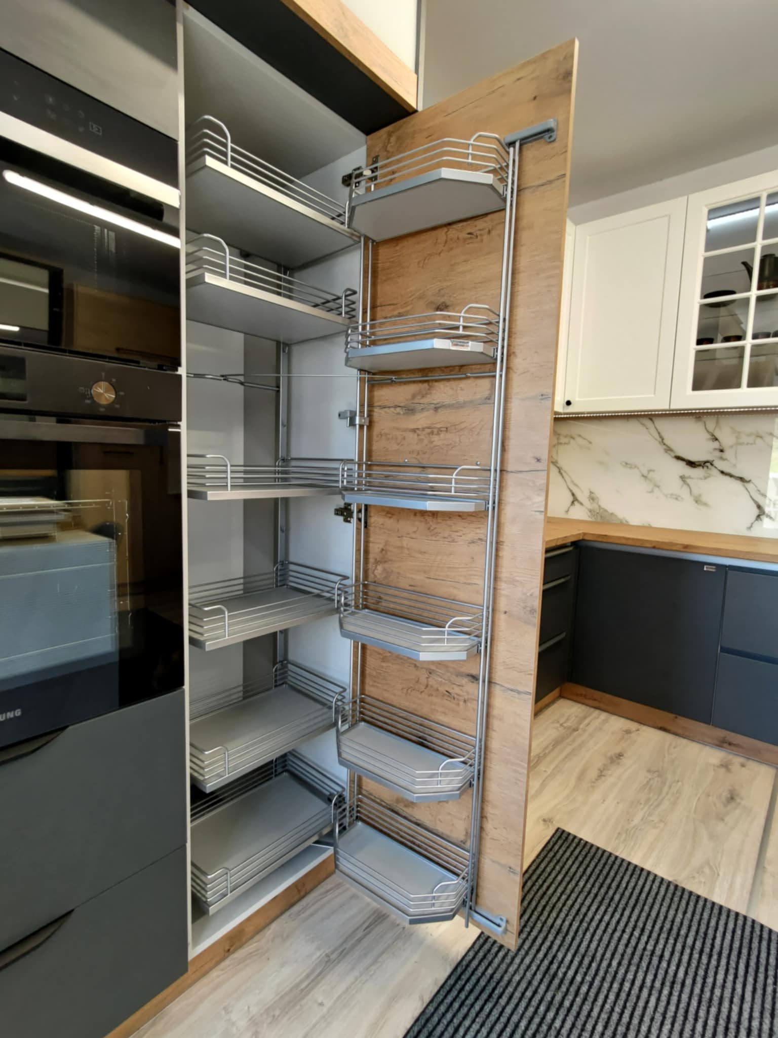 Nowoczesna kuchnia z szufladami cargo w szafce, drewnopodobny front, szare szafki dolne i białe górne, marmurowy backsplash, widok z bliska na system przechowywania.