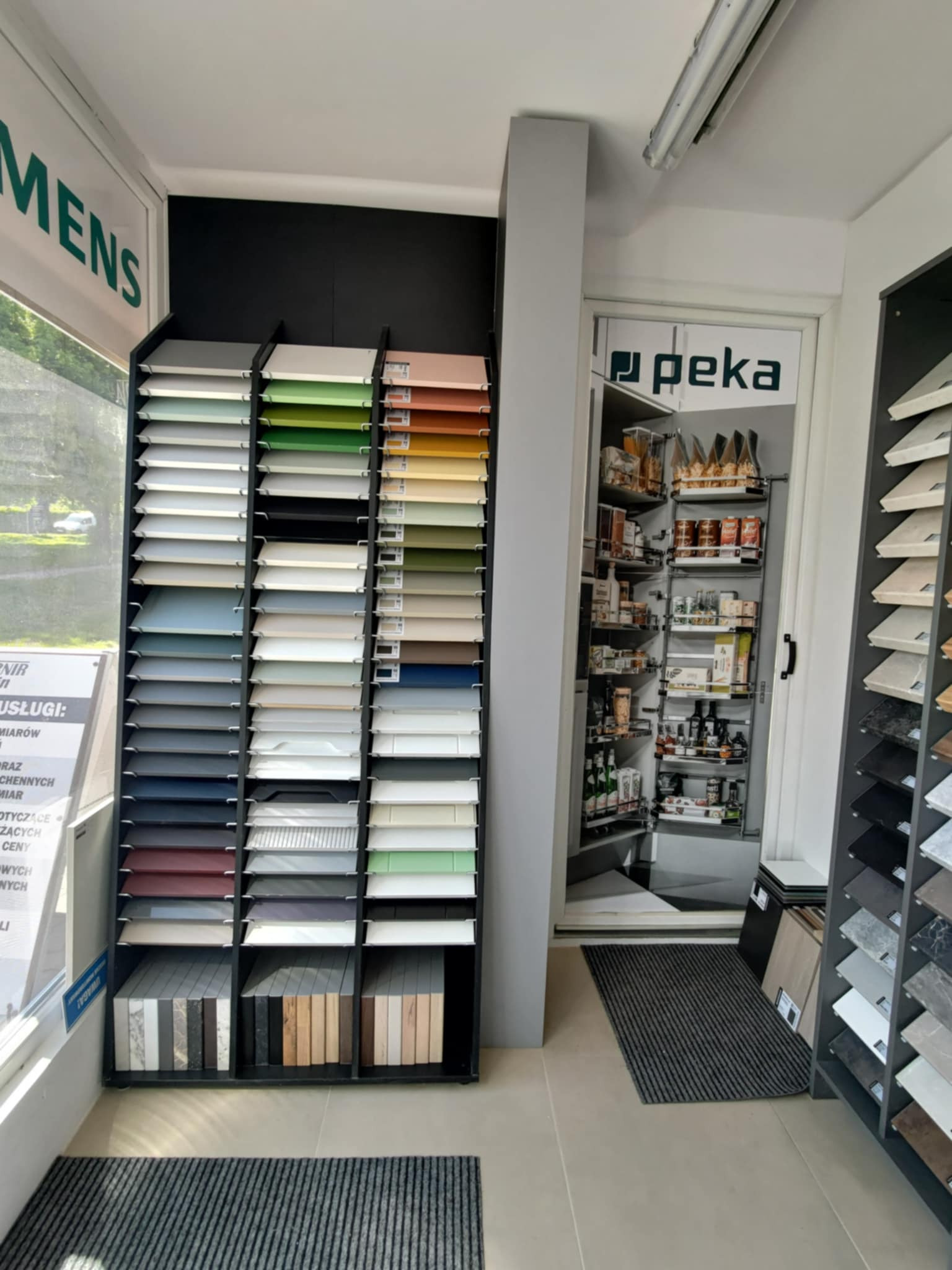 Ekspozycja próbek blatów i frontów meblowych w salonie, obok wysuwana szafka cargo Peka. Prezentacja materiałów wykończeniowych do kuchni na wymiar.
