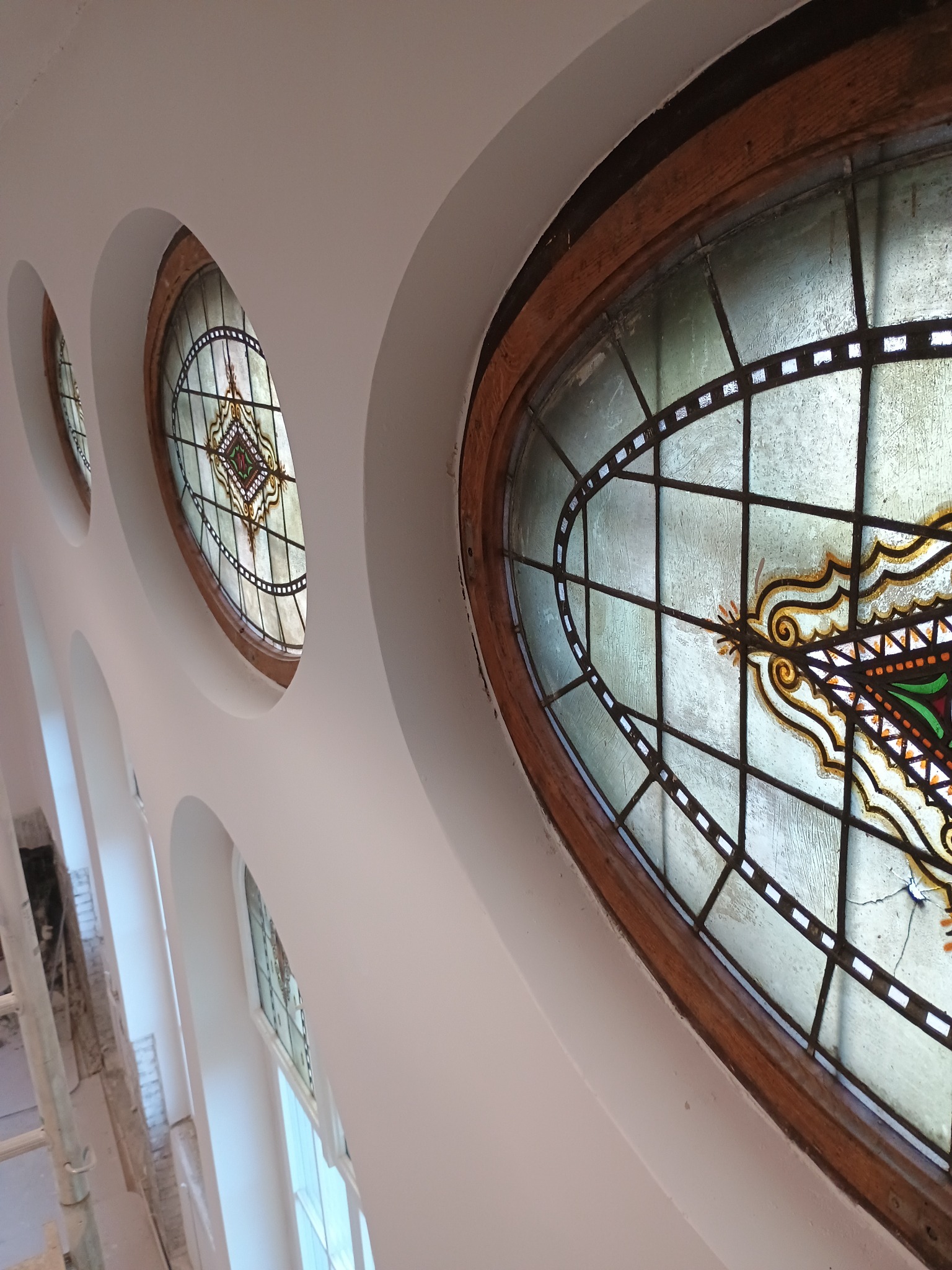 Białe sklepienie z owalnymi oknami witrażowymi w drewnianych ramach. Widok z dołu, ukośny kadr. W tle rusztowanie.
