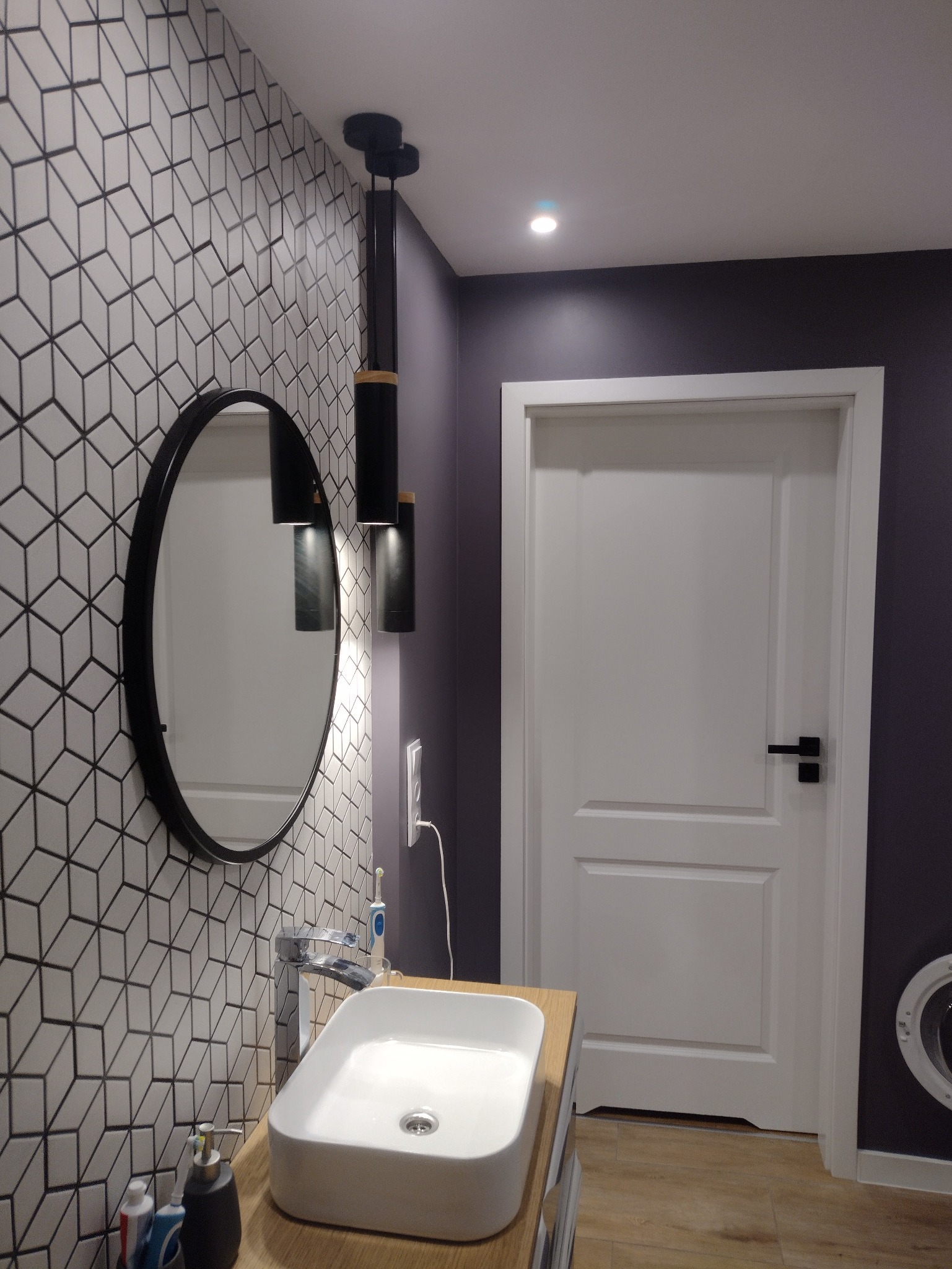 Nowoczesna łazienka po remoncie: biała umywalka nablatowa, lustro w czarnej ramie i geometryczne płytki na ścianie. Minimalistyczne oświetlenie.