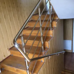 Drewniane schody z błyszczącą, metalową konstrukcją zabezpieczającą w domu w Miejscu Piastowym, widok z góry.