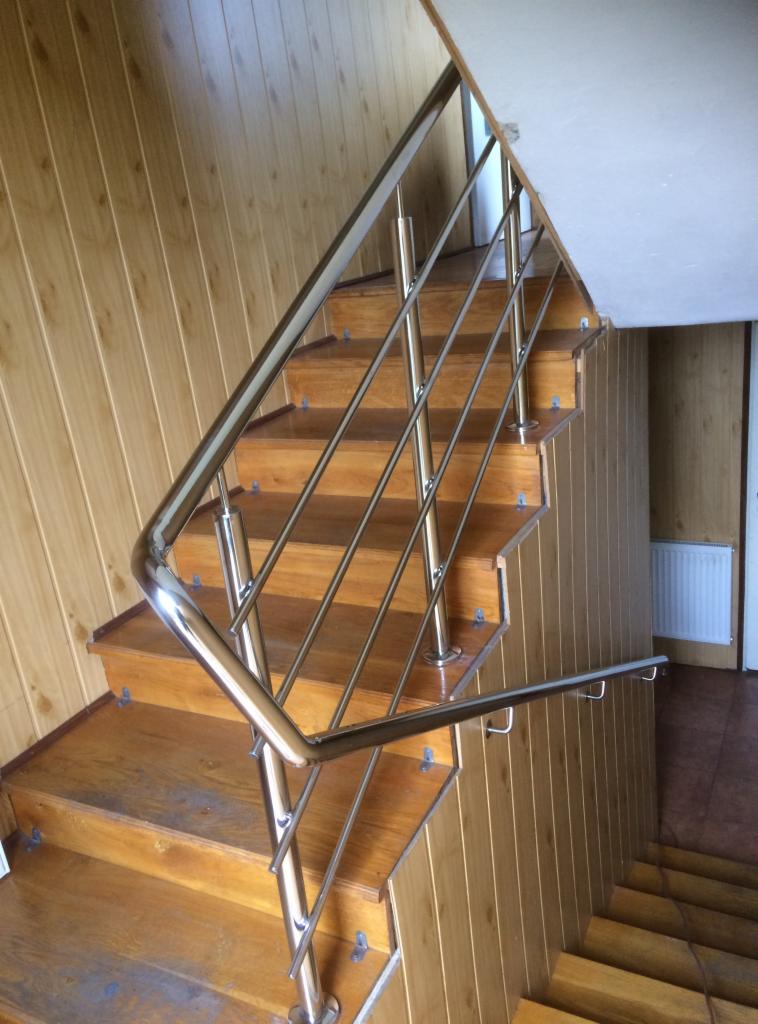 Drewniane schody z błyszczącą, metalową konstrukcją zabezpieczającą w domu w Miejscu Piastowym, widok z góry.